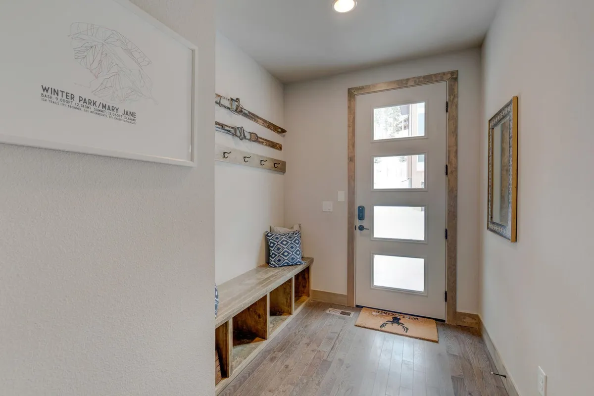 A bright, welcoming entryway featuring a stylish front door, a practical bench for putting on or removing shoes, wall hooks perfect for hanging outdoor gear, and a decorative mirror. The space is designed to greet guests and handle the transition between outdoor adventure and indoor relaxation.