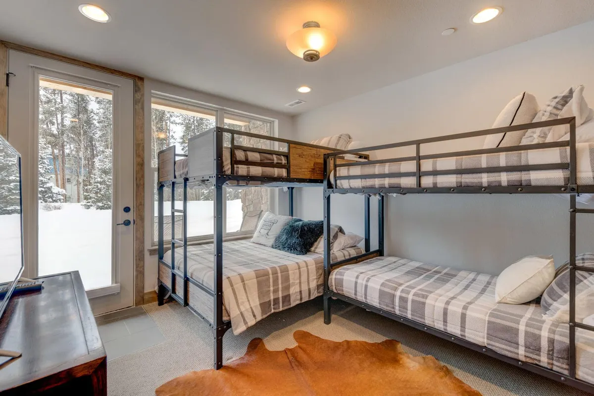 A bright and playful bunk room featuring two sets of bunk beds with soft bedding, large windows letting in natural light, and sturdy wooden furniture. The space is clearly designed for fun and flexibility, suitable for children or groups.