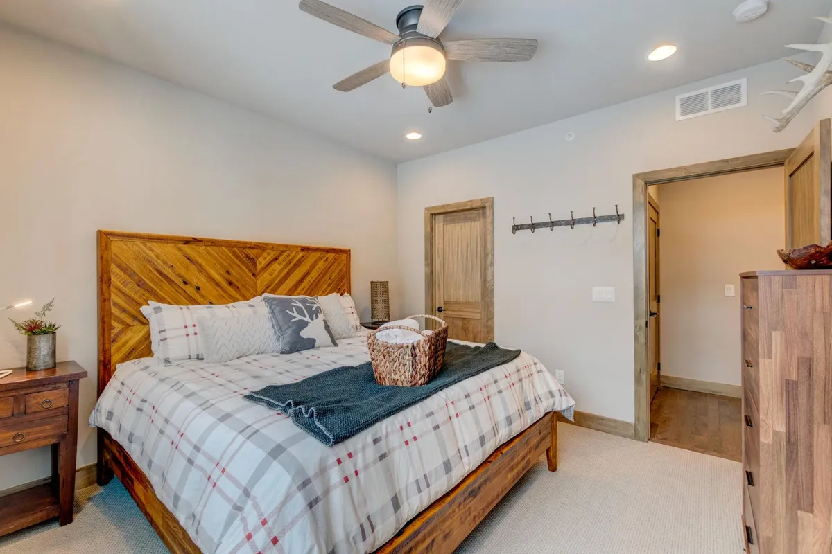 A comfortable bedroom with a wooden bed frame, plaid bedding, a decorative throw blanket, a nightstand topped with a potted plant, and inviting doorways leading to other parts of the suite. The mood is serene, ideal for unwinding after a day of adventure.