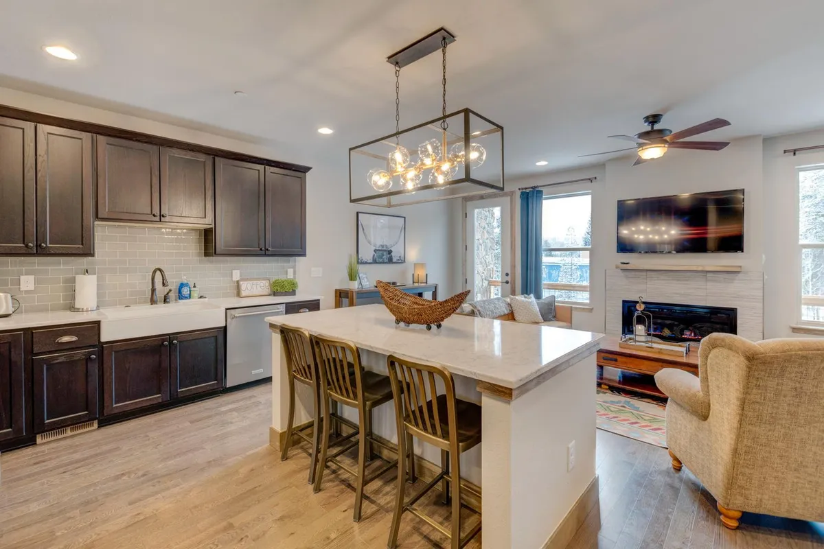 A wider shot showing the kitchen island, chandelier, and an adjoining living area with a TV and comfortable seating. This perspective reveals the seamless integration between the kitchen, dining, and living spaces—underscoring the open layout that keeps the chef part of the action during gatherings.