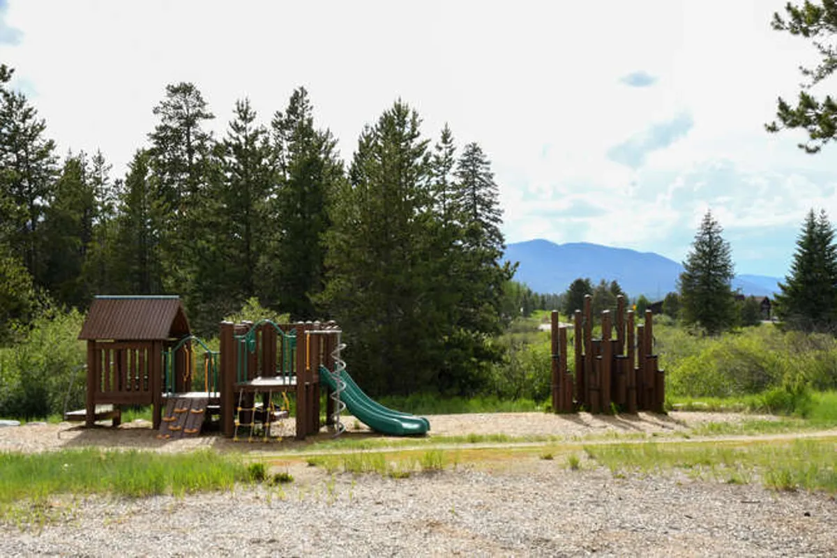 A lively outdoor playground set amid trees, featuring slides, climbing structures, and open areas for children to play. Families can be seen gathered around, with kids engaged in energetic activities, creating a vibrant scene of laughter and connection.