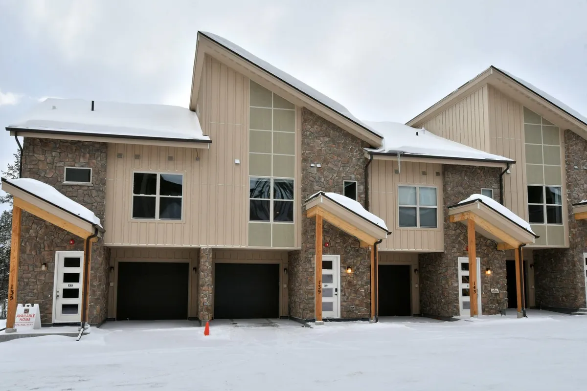 The villa’s exterior showcases a striking stone facade, angled roofs, and wooden accents, all set amidst a winter landscape. Snow blankets the ground and the home’s entryway, while warm light glows from inside, creating a welcoming and high-end impression. The setting hints at both solitude and togetherness, perfect for family gatherings or romantic escapes.