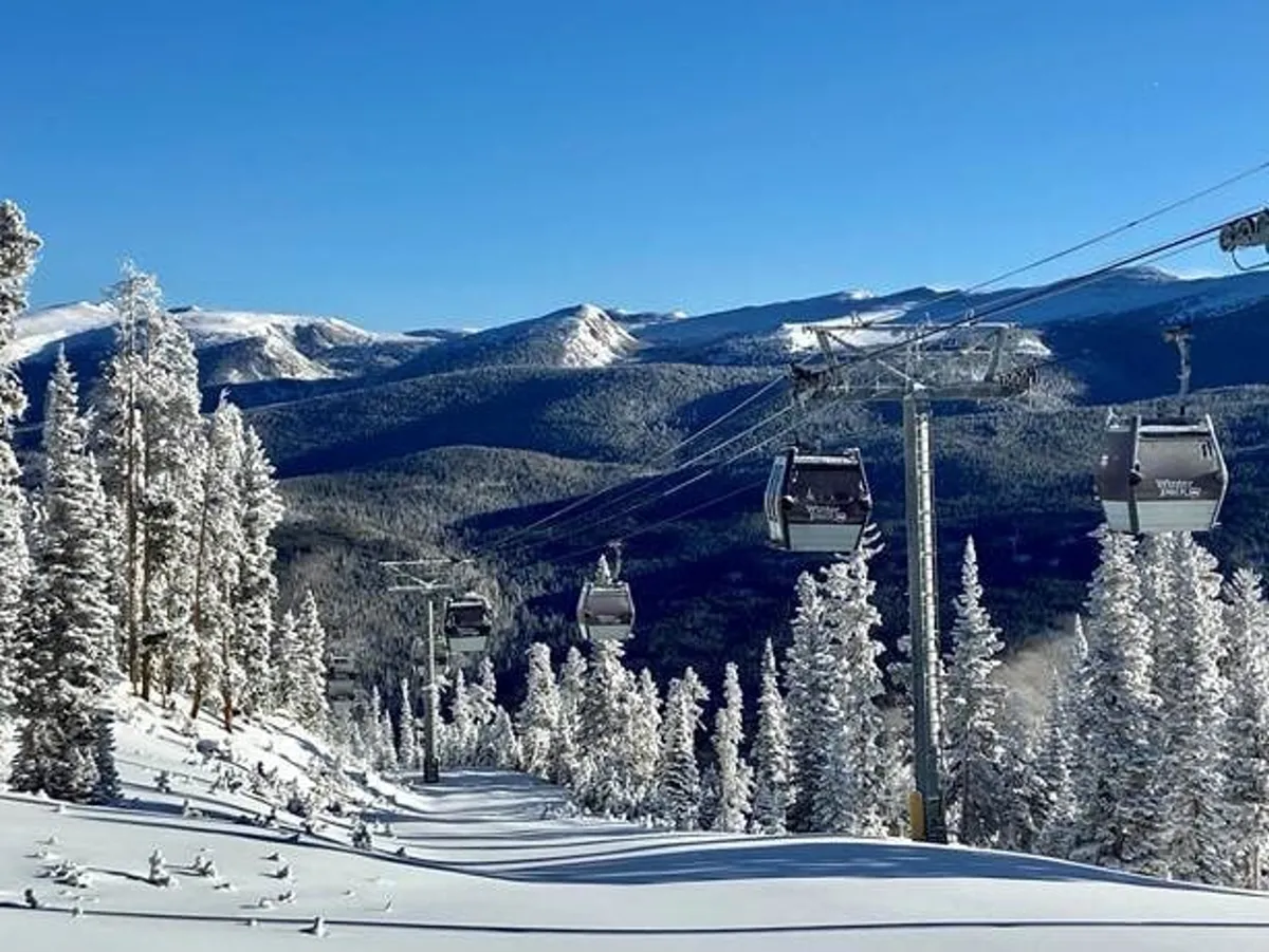 A panoramic exterior view of a gondola lift ascending snow-covered slopes surrounded by pine trees and mountains. The scene captures people skiing and snowboarding, all set in a tranquil, picturesque winter landscape.
