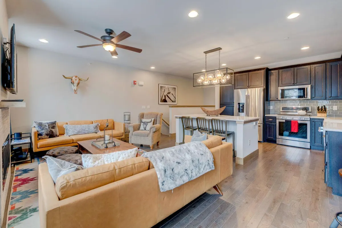 An open-concept living and dining space with elegant sofas, a striking fireplace, and a dining area visible in the background. The kitchen island is also partially in view, emphasizing the flow between spaces. Warm lighting and thoughtfully placed decor contribute to a welcoming ambiance suited for sharing meals and stories.