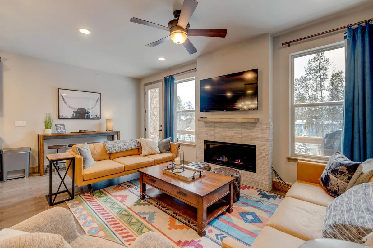 A comfortable living space with a plush sofa, a coffee table ready for board games, and large windows that frame beautiful mountain views. The TV is positioned for easy viewing, while the overall decor is warm and inviting. The windows emphasize the connection to the Rockies just outside.