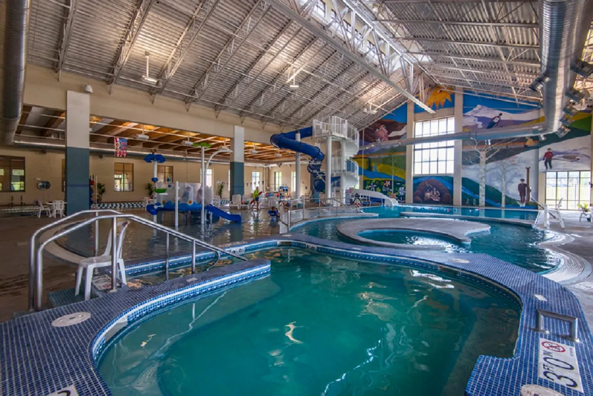 An indoor aquatic center bustling with activity, showcasing a colorful water slide, play features, and pools. Children and parents enjoy the excitement of the water attractions, highlighting the variety of recreational options available.