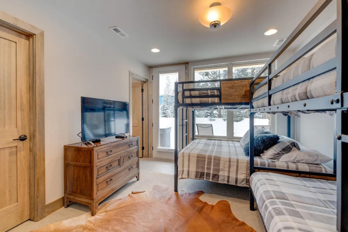 A versatile bedroom with built-in bunk beds, a TV, a wooden dresser, and large windows. The environment is both cozy and functional, ideal for movie nights or playtime, and the TV highlights the tech amenities available in select bedrooms.